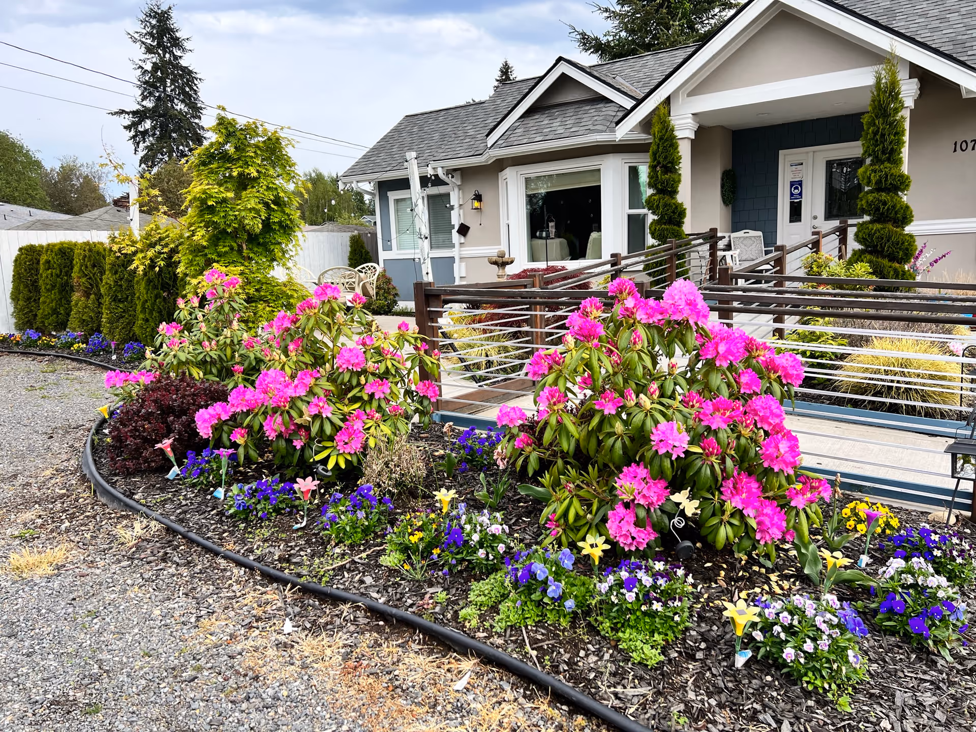 Exterior of a senior living facility with a flowering garden and wooden railing.