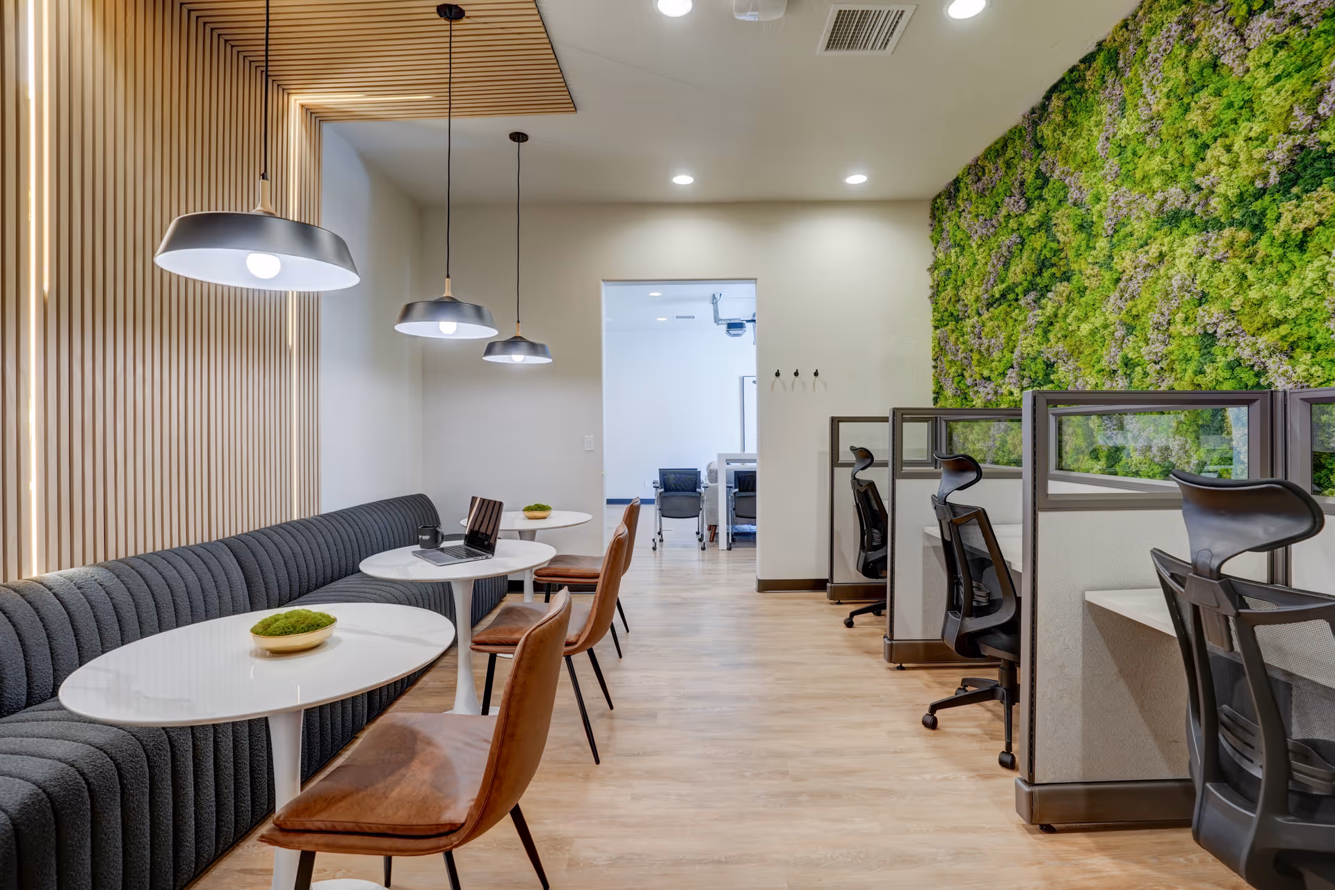Modern senior living facility lounge featuring round tables, a gray sofa, leather chairs, and workstations.