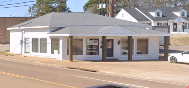 White single-story At Home Healthcare building on street with front porch and large windows.