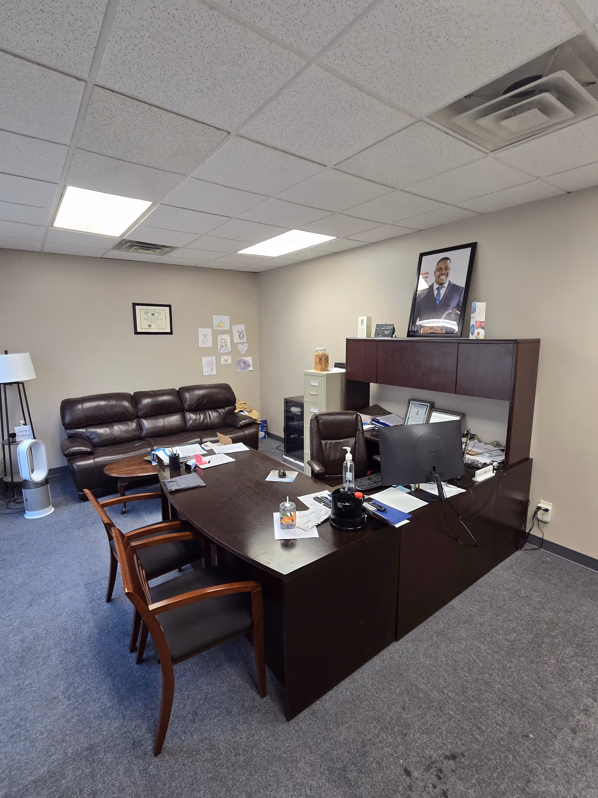 Office desk area with chairs, computer, and leather sofa in a senior care office.
