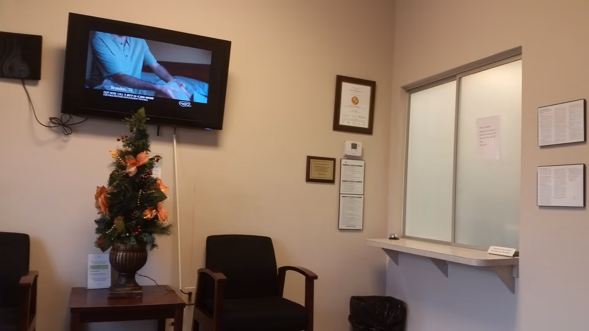 Lobby seating area with a wall-mounted TV, plant centerpiece, and service window.