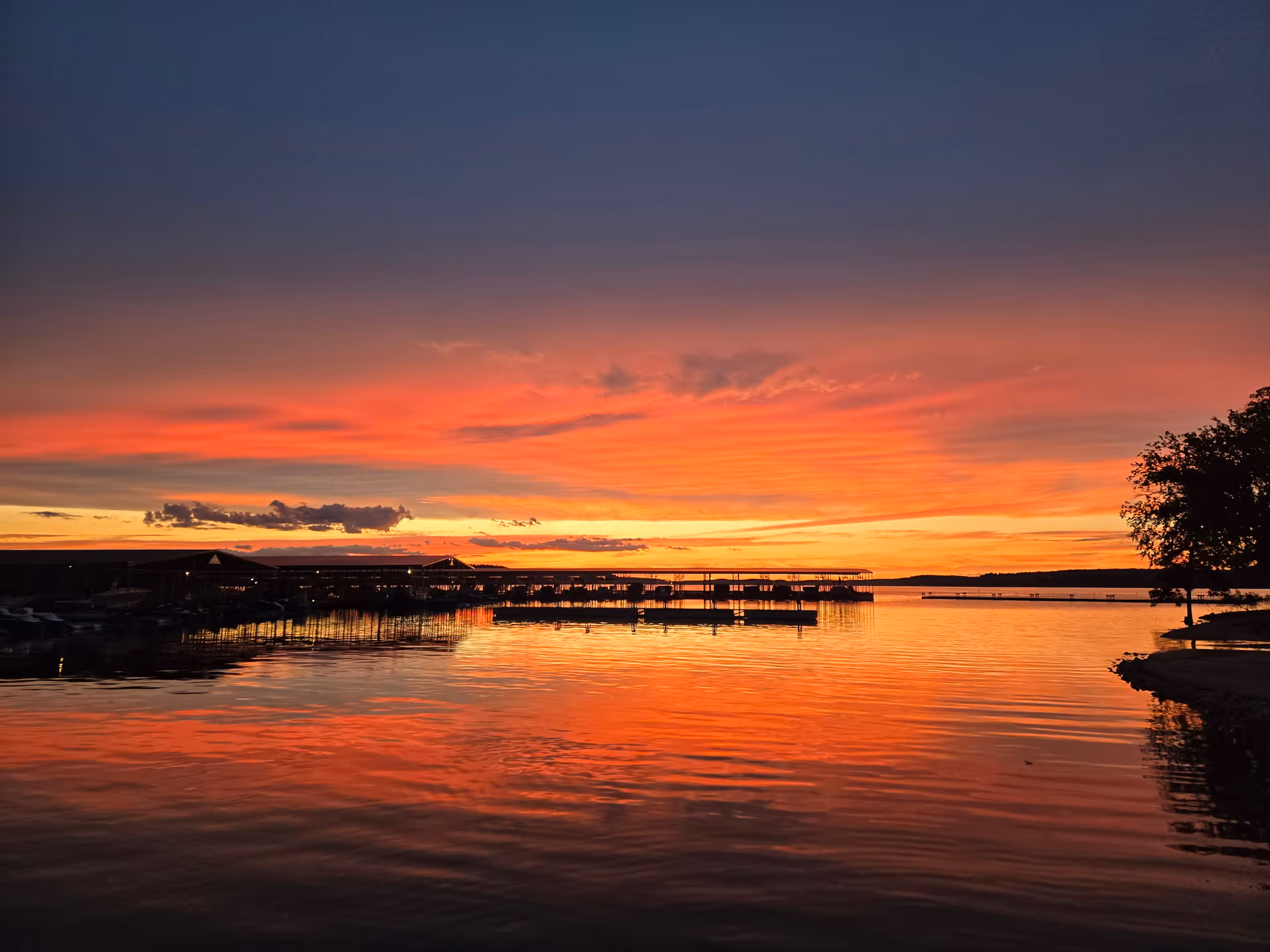 Sunset over a calm lake with docks and silhouetted trees.