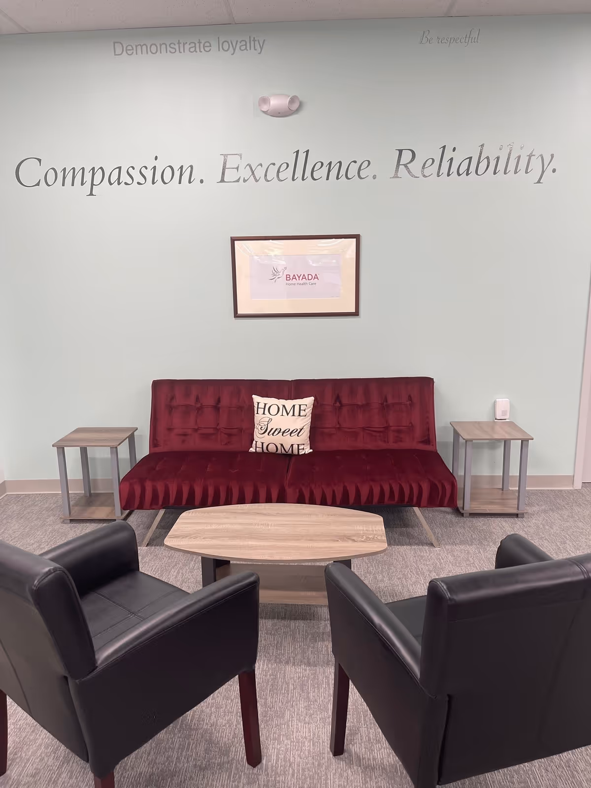 A burgundy sofa with two side tables and black chairs in a pale lounge area.