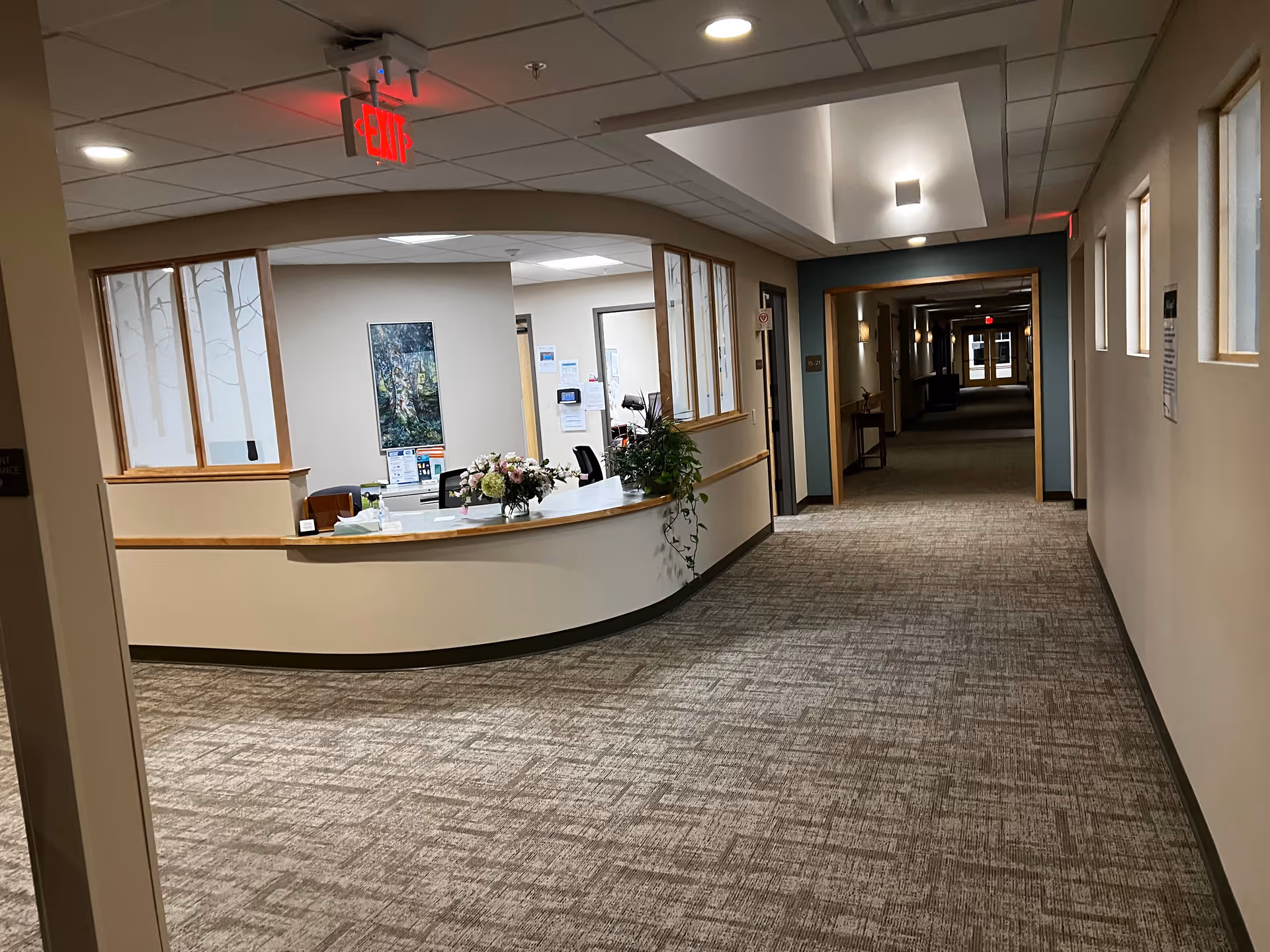 Interior hallway of a senior facility with a curved reception desk and plants.