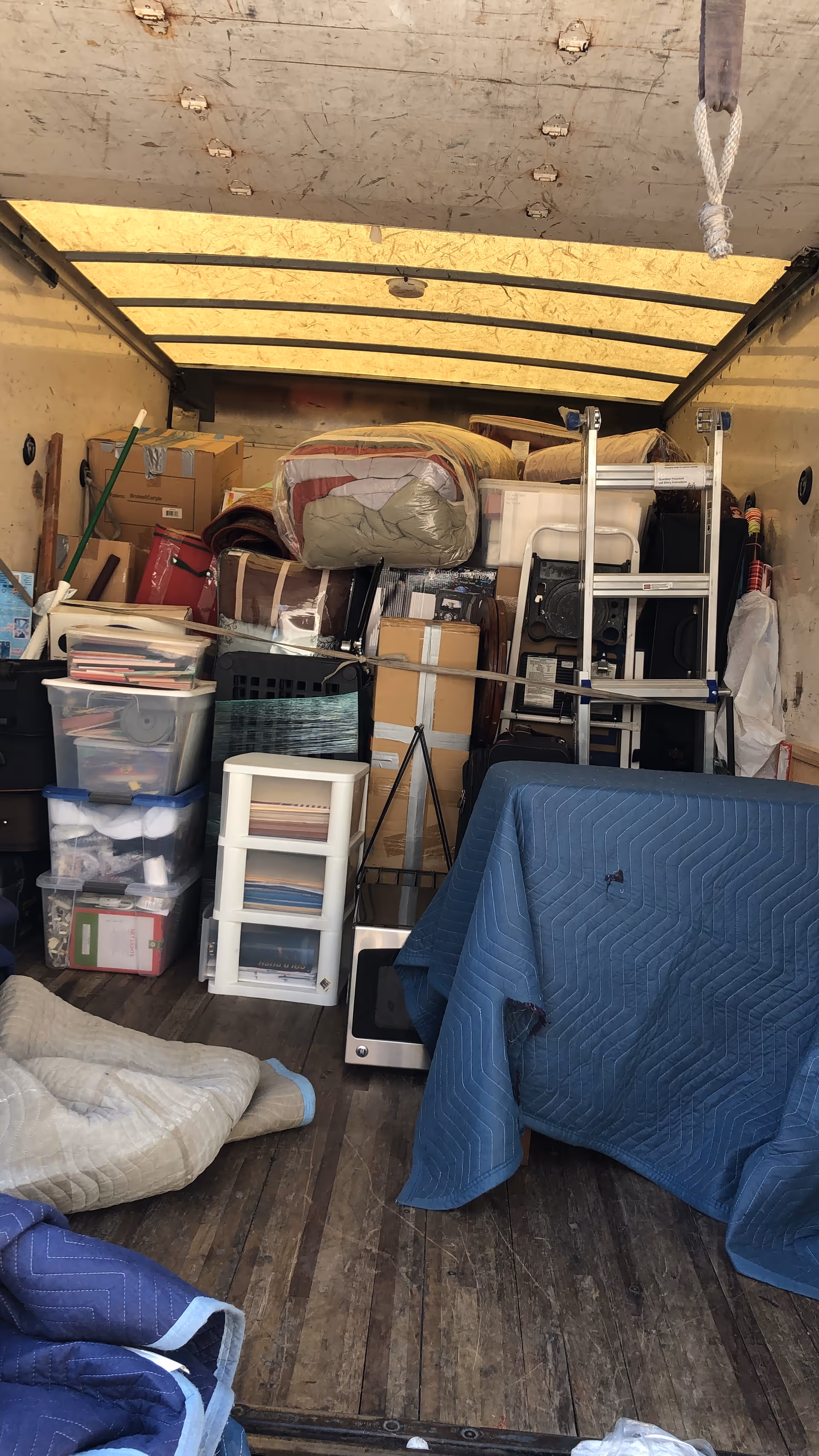 Cluttered interior storage area with stacked boxes, furniture, and covered items in a facility.