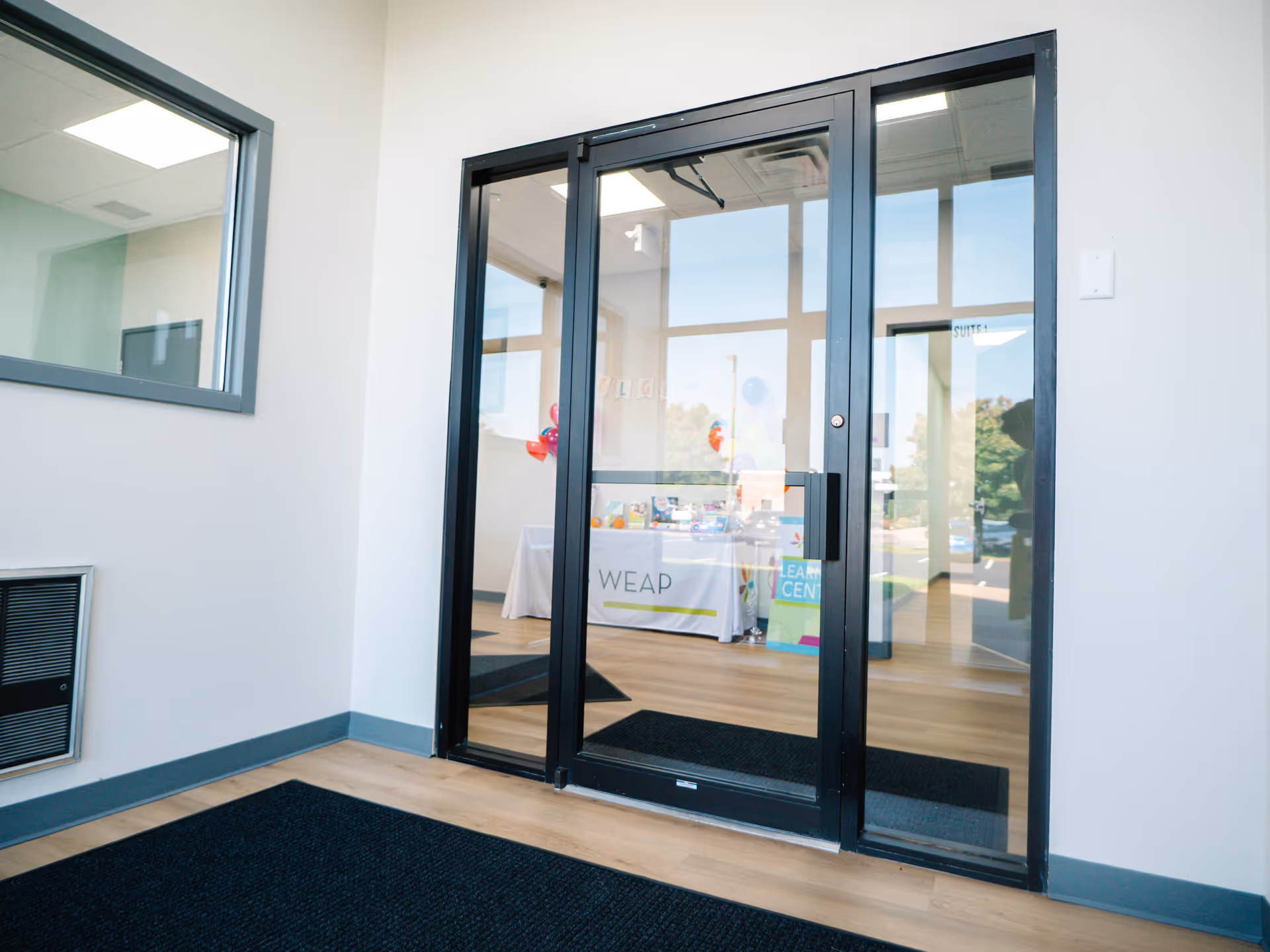 Glass double doors lead into a bright reception area with WEAP signage inside.