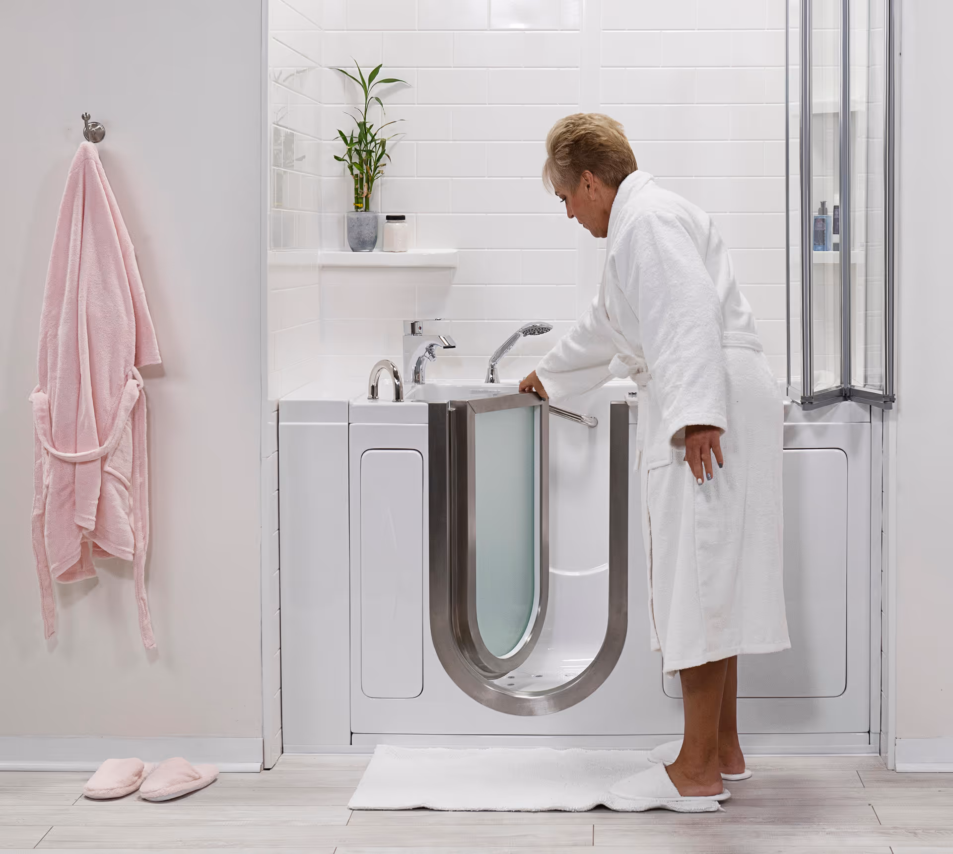 A person in a white robe uses a modern walk-in tub in a bright bathroom.