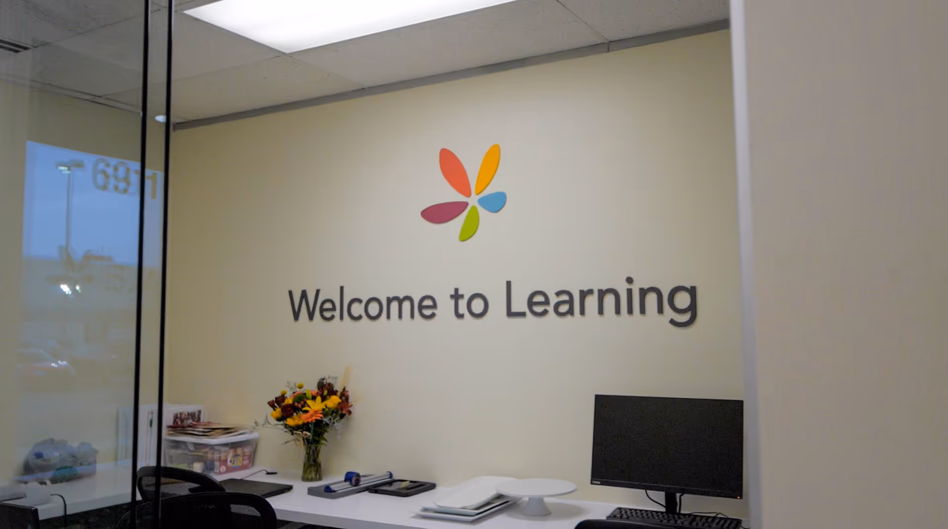 Reception area with computer, flowers, and a Welcome to Learning wall sign.