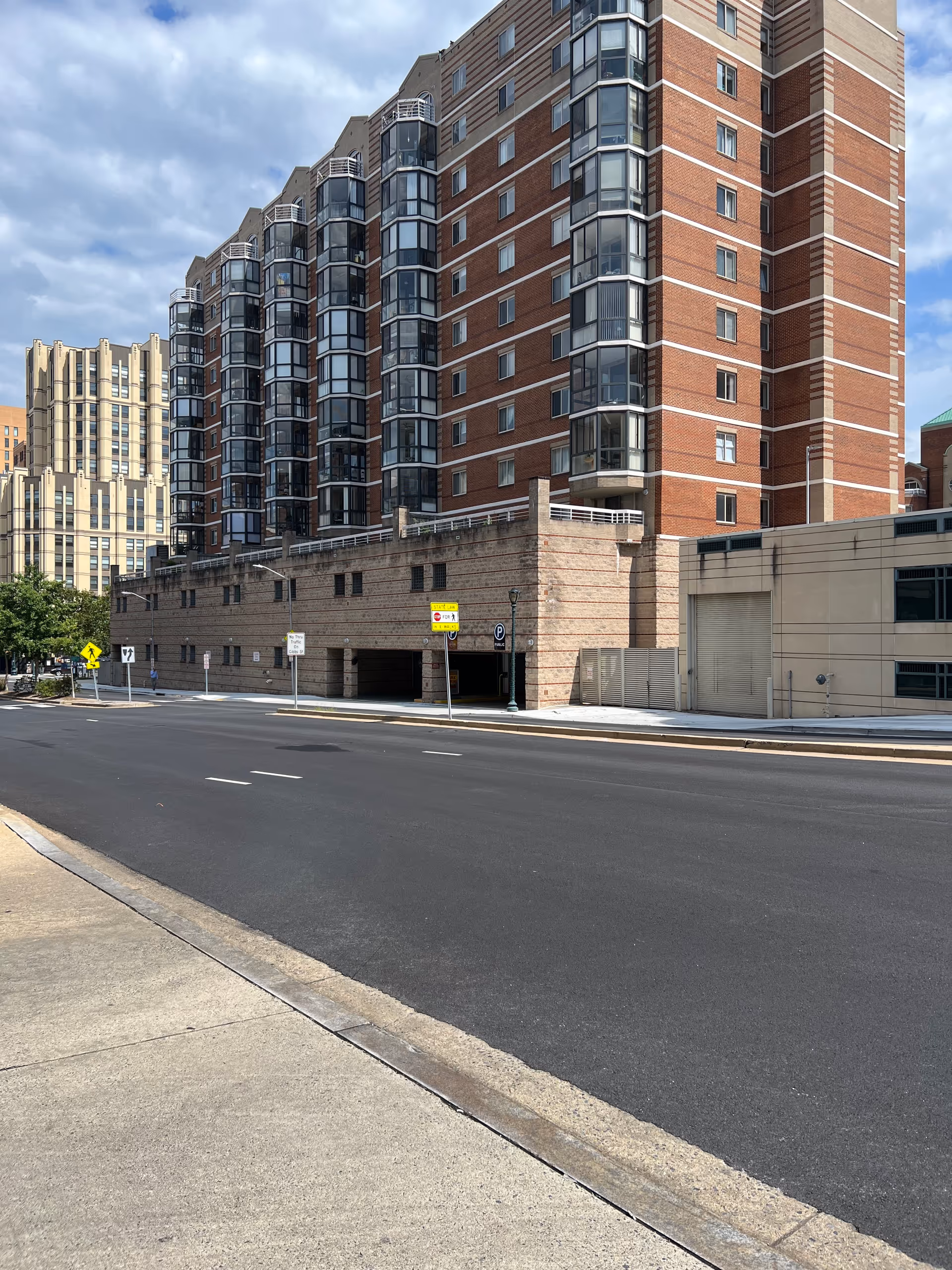 Tall brick apartment building rises along a city street with a parking entrance below.