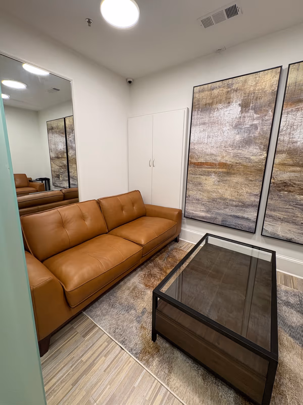 Brown leather sofa, glass coffee table, and large abstract art panels in a modern lounge.