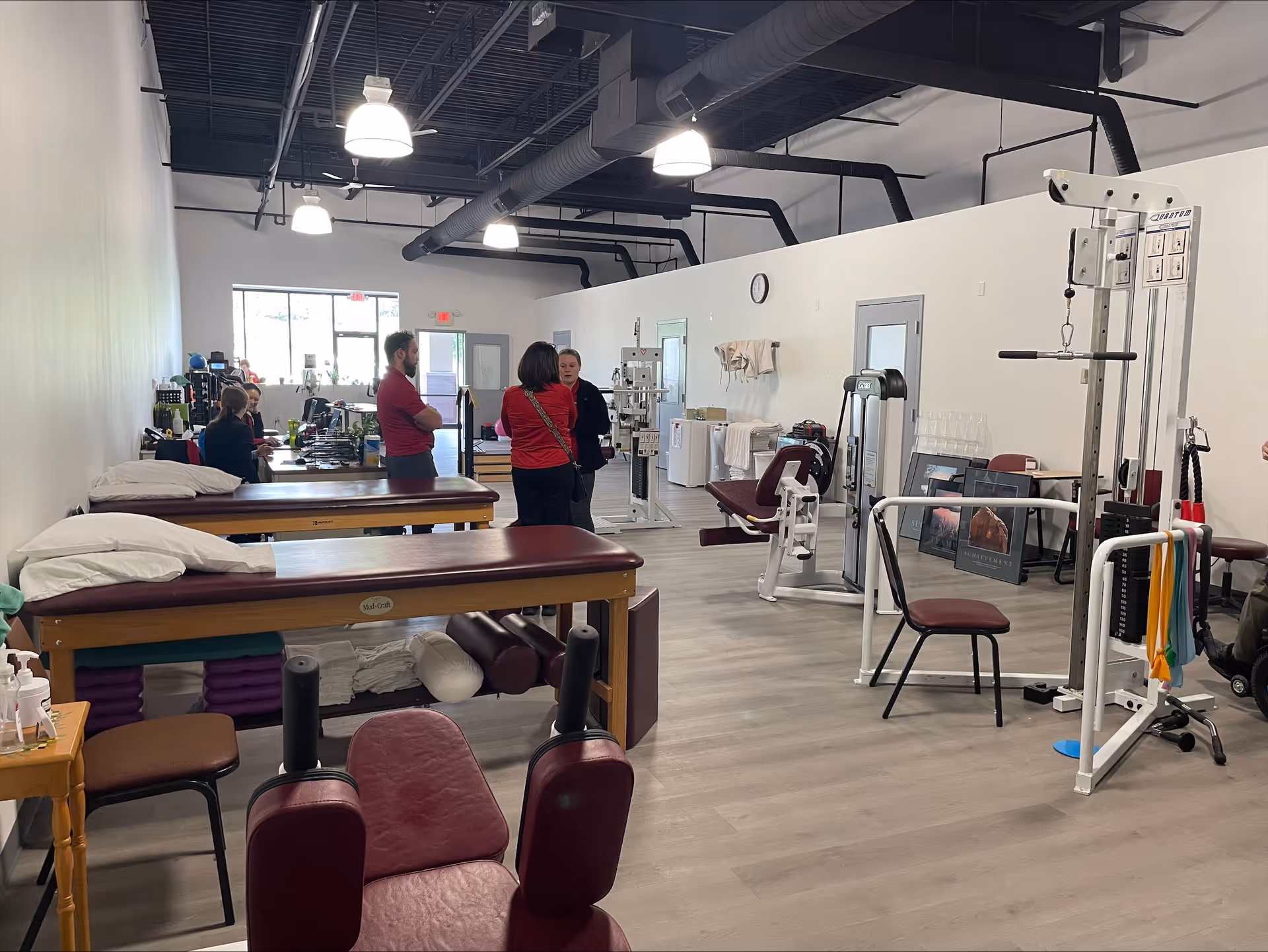 Interior physical therapy gym with equipment and people conversing.