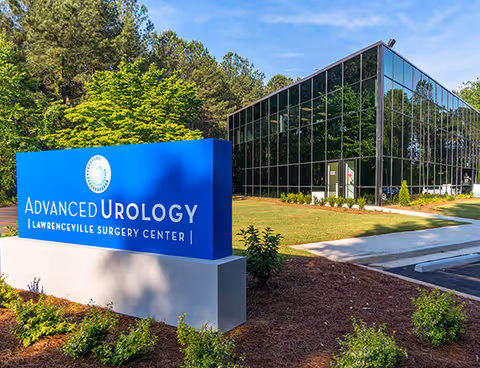 Blue Advanced Urology sign beside a modern glass building with landscaped entry.