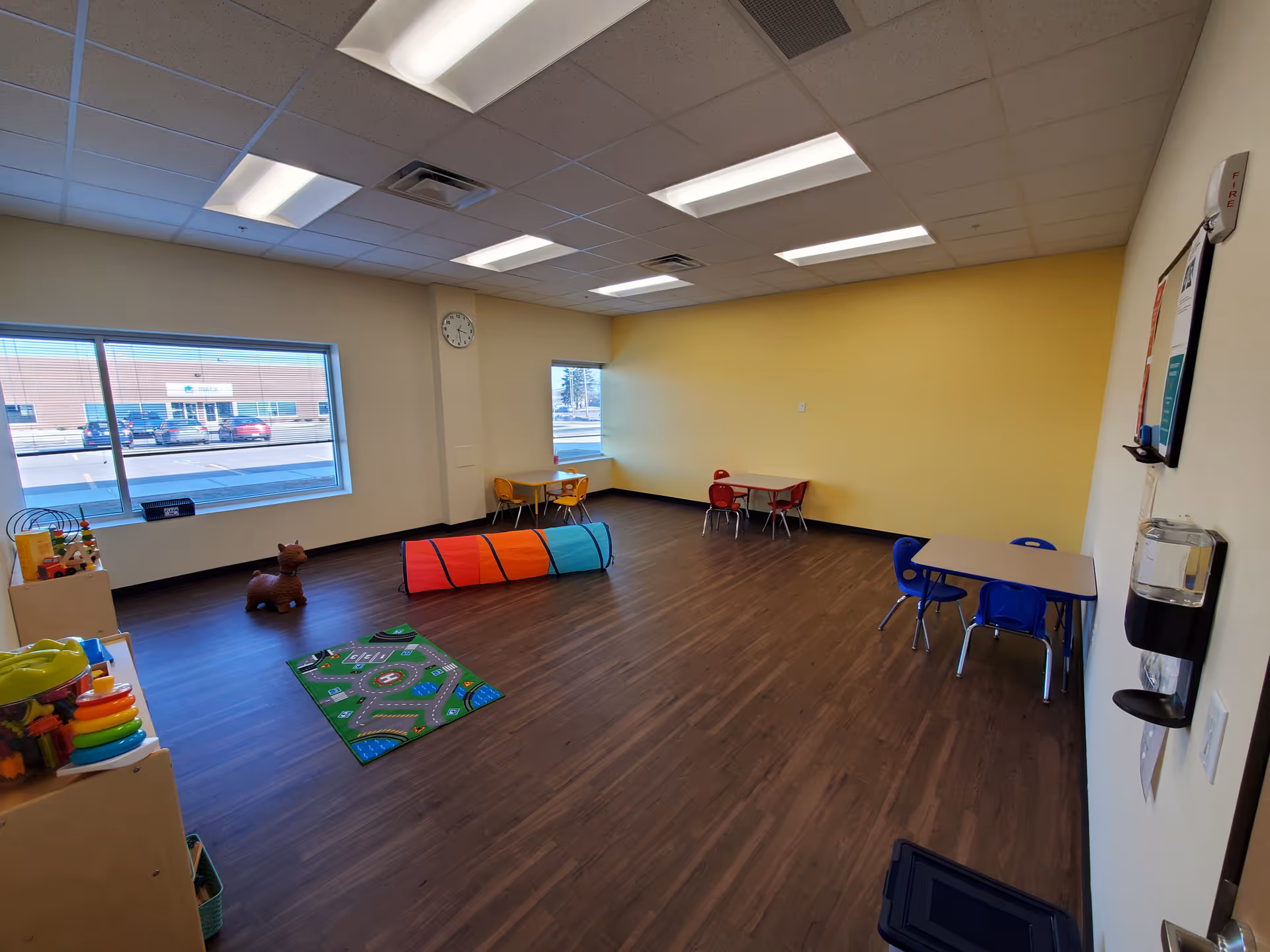 Colorful children's playroom with small tables, toys, tunnel, and wood flooring.