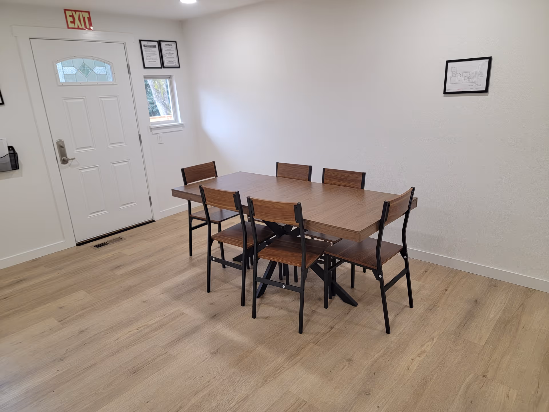 A simple dining room with a wooden table and six chairs in a bright, minimal space.
