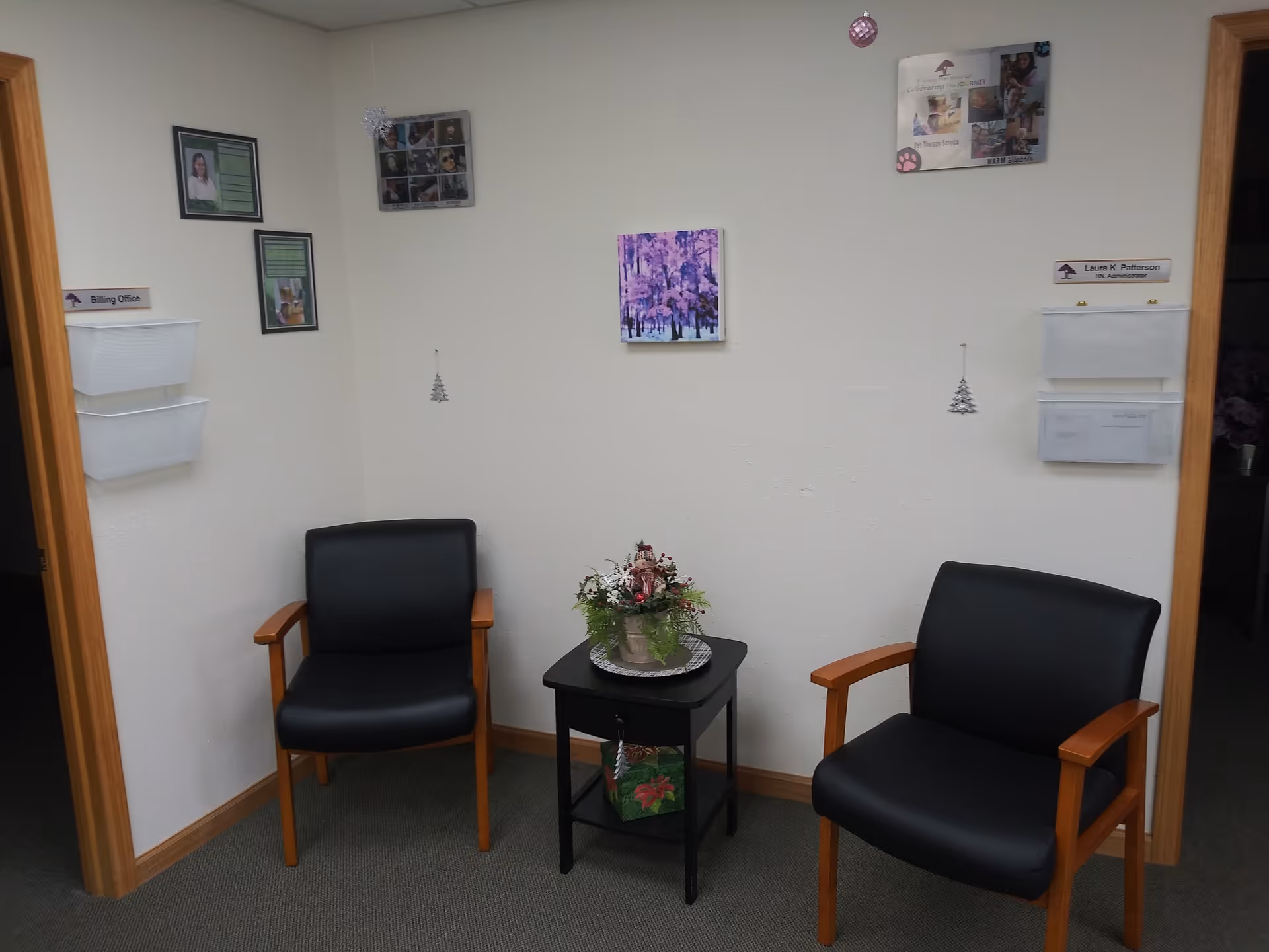 Two black armchairs flank a small table with a flower arrangement in a quiet waiting area.