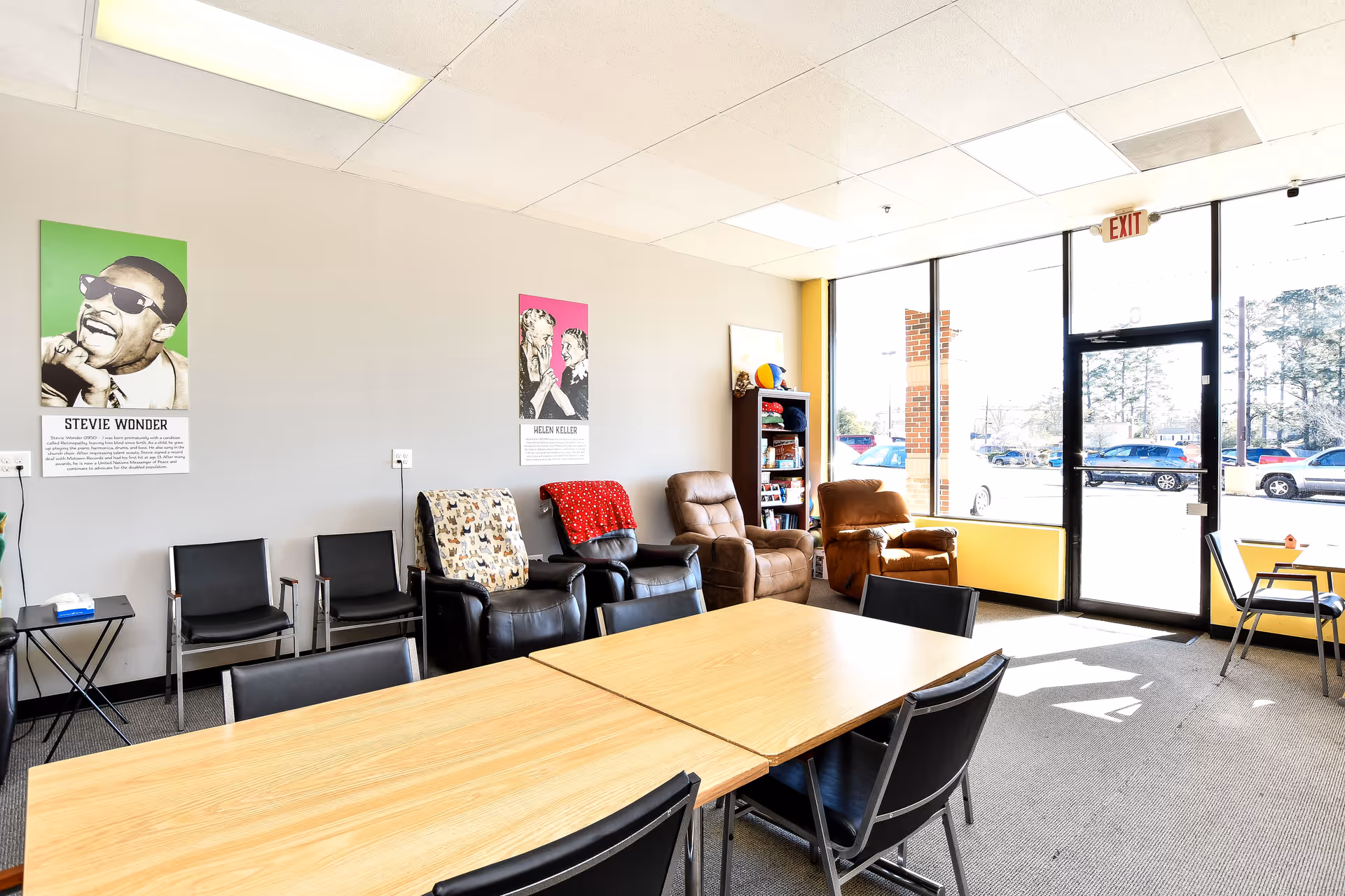 Bright interior common area with a long table, chairs, and lounge seating near glass doors.