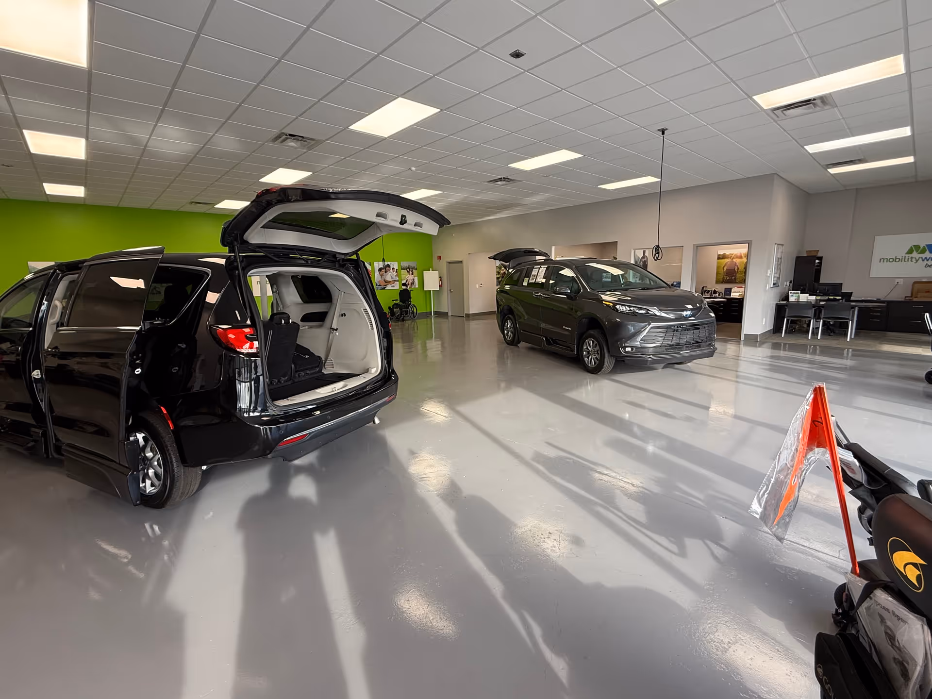 Indoor mobility showroom with multiple vehicles and an open hatch near a lime wall.
