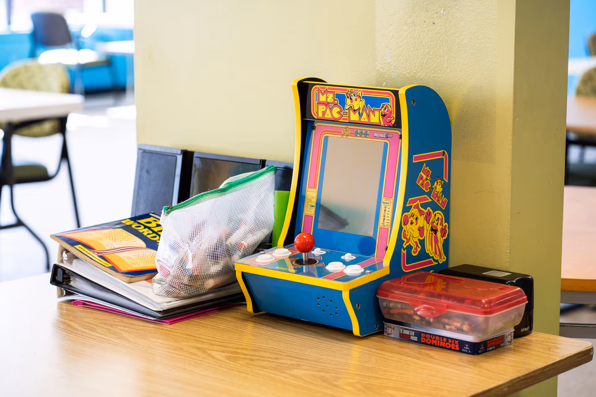 Colorful tabletop arcade game sits on a wooden table in a bright indoor lounge.