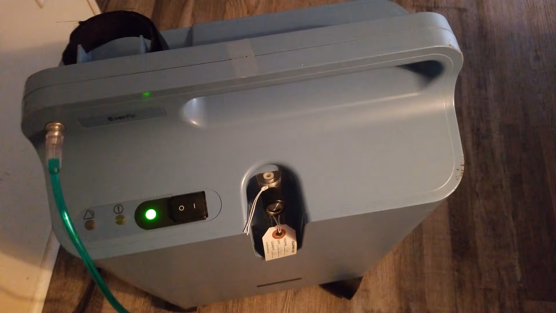 Blue-gray Everflo portable oxygen concentrator with green tubing on a wooden floor.