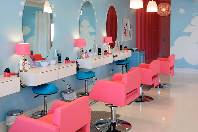 Bright salon interior with pink chairs, blue stations, and mirrors along a light blue wall.