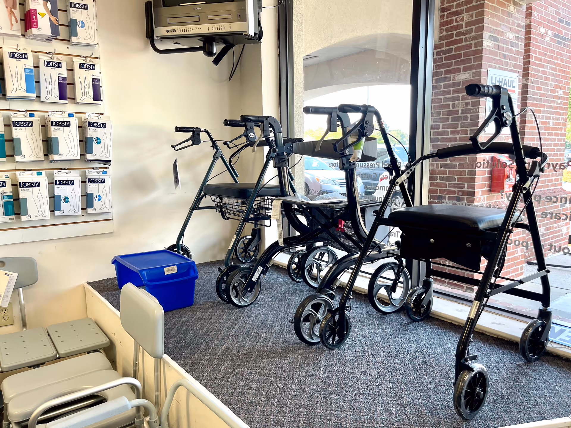 Rows of walkers and mobility aids near a display and window in a medical supply area.