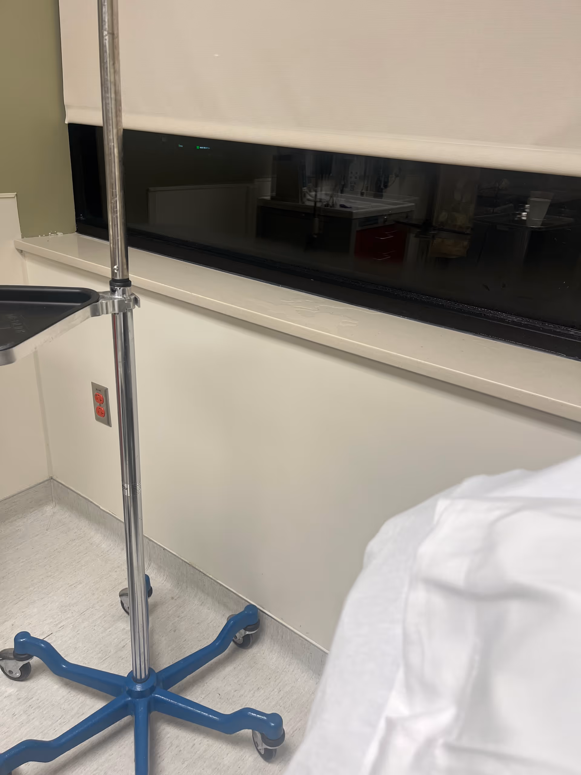 Hospital room interior with an IV stand near a window and bed sheet.