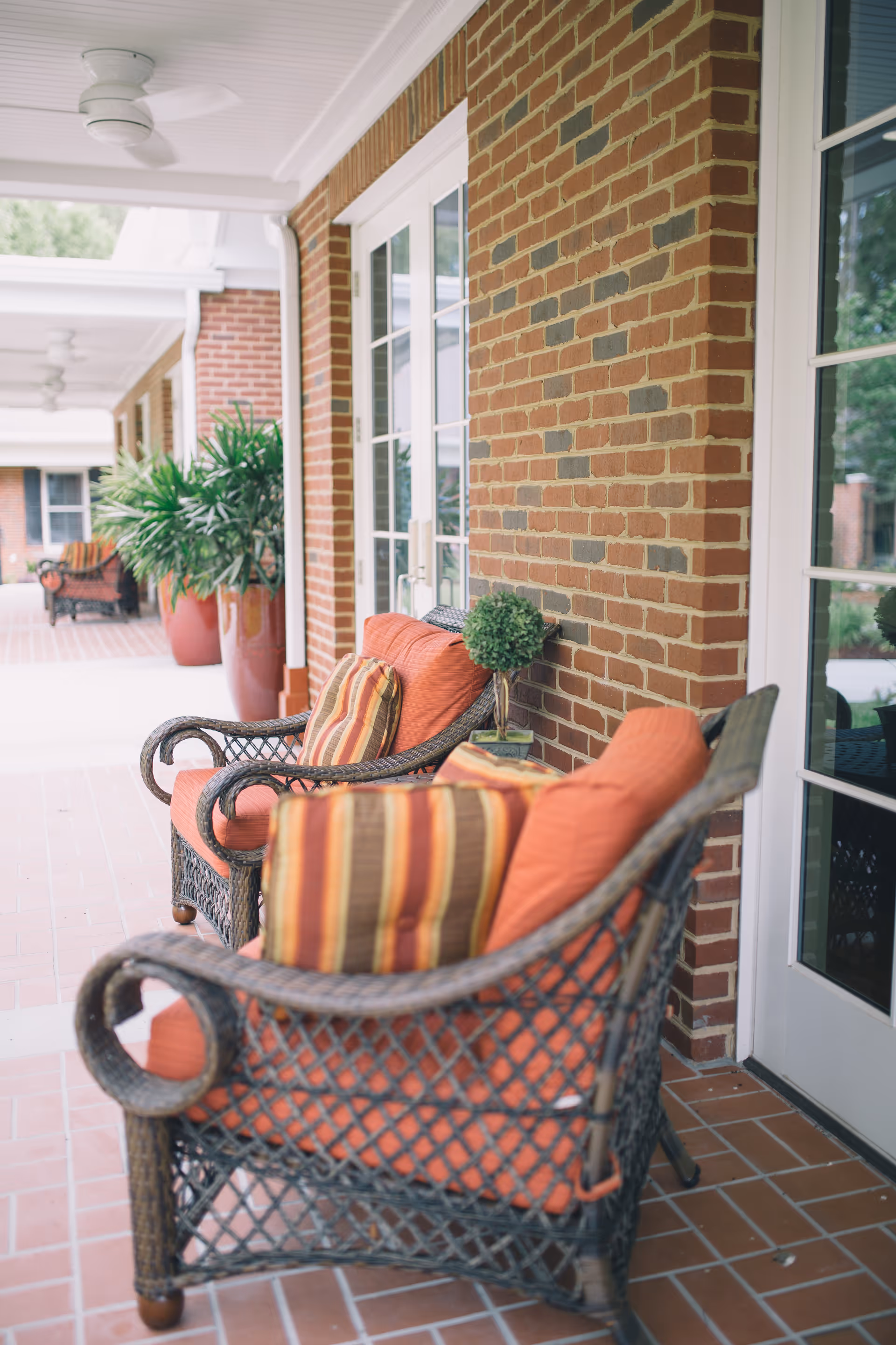 Porch seating area with wicker chairs and orange cushions along a brick building.