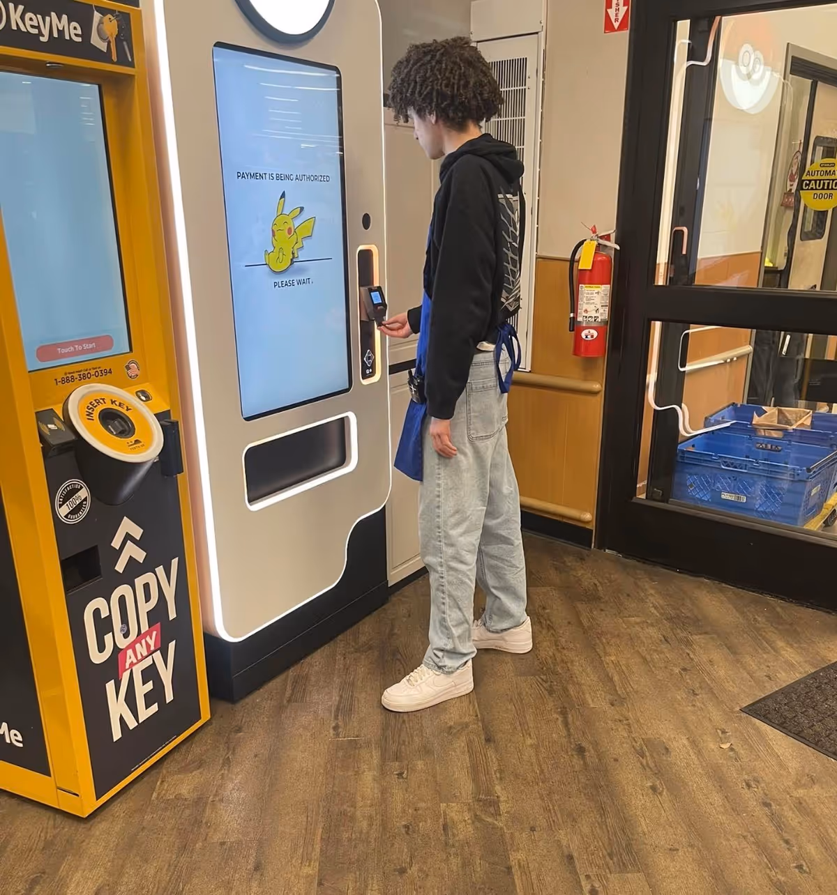 A person uses a touchscreen kiosk beside a key-copy machine inside a store.