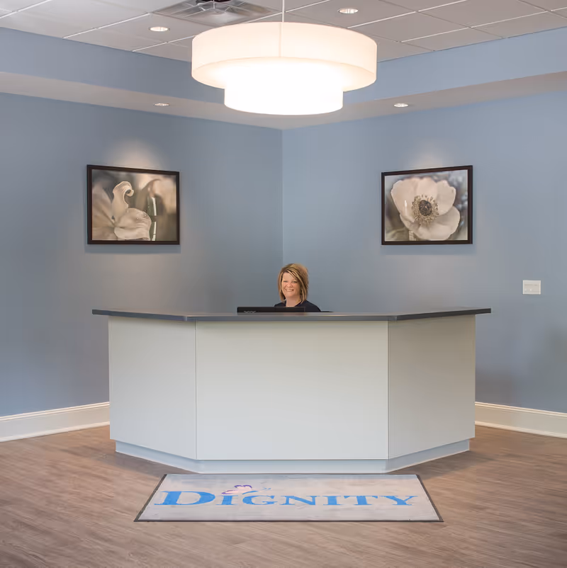 Dignity Hospice lobby reception with curved white desk and smiling attendant