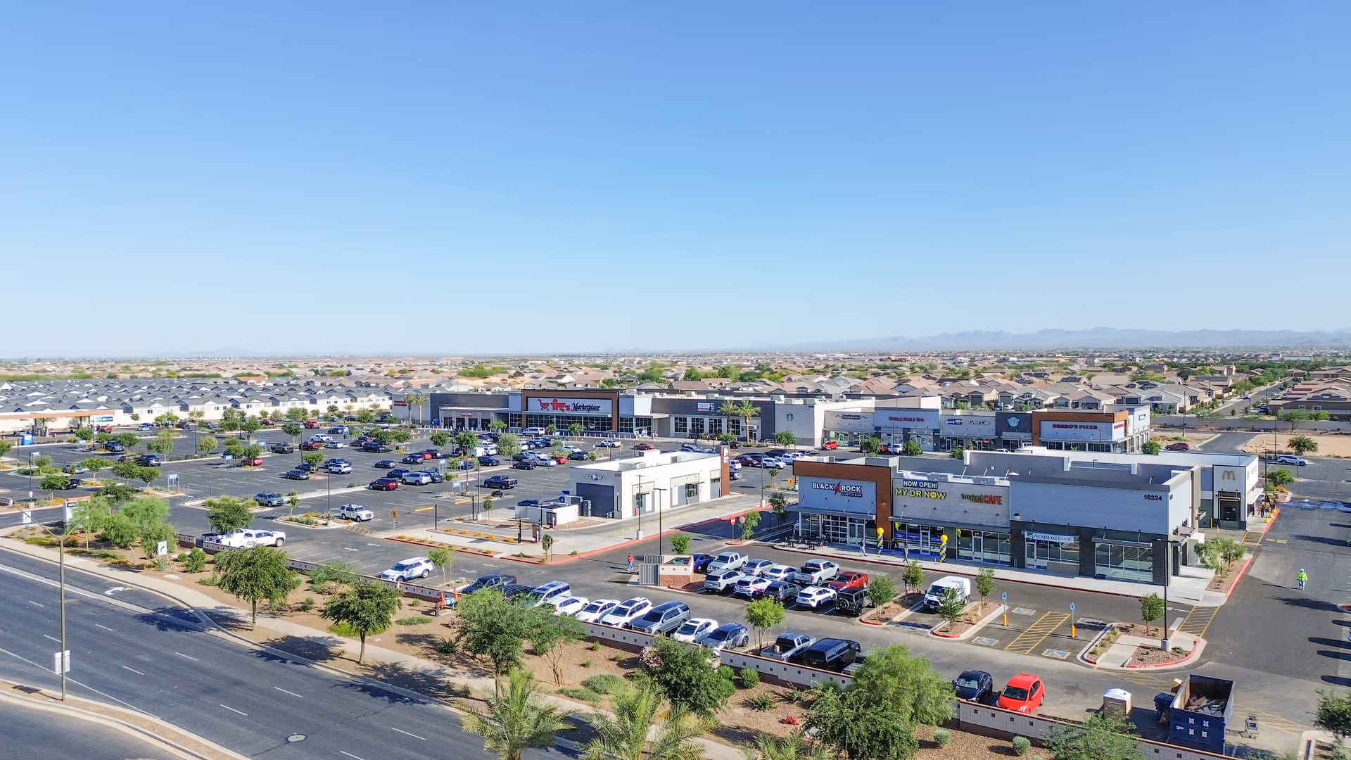 Aerial view of a suburban shopping center with multiple storefronts and a large parking lot.