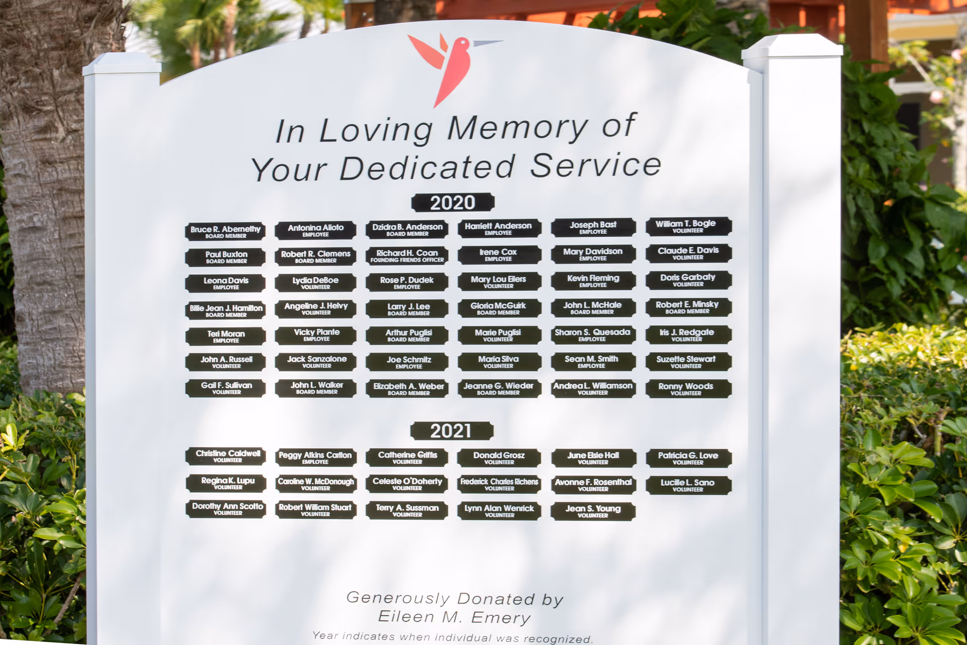 A large white outdoor memorial signboard listing donor plaques with 'In Loving Memory' message.