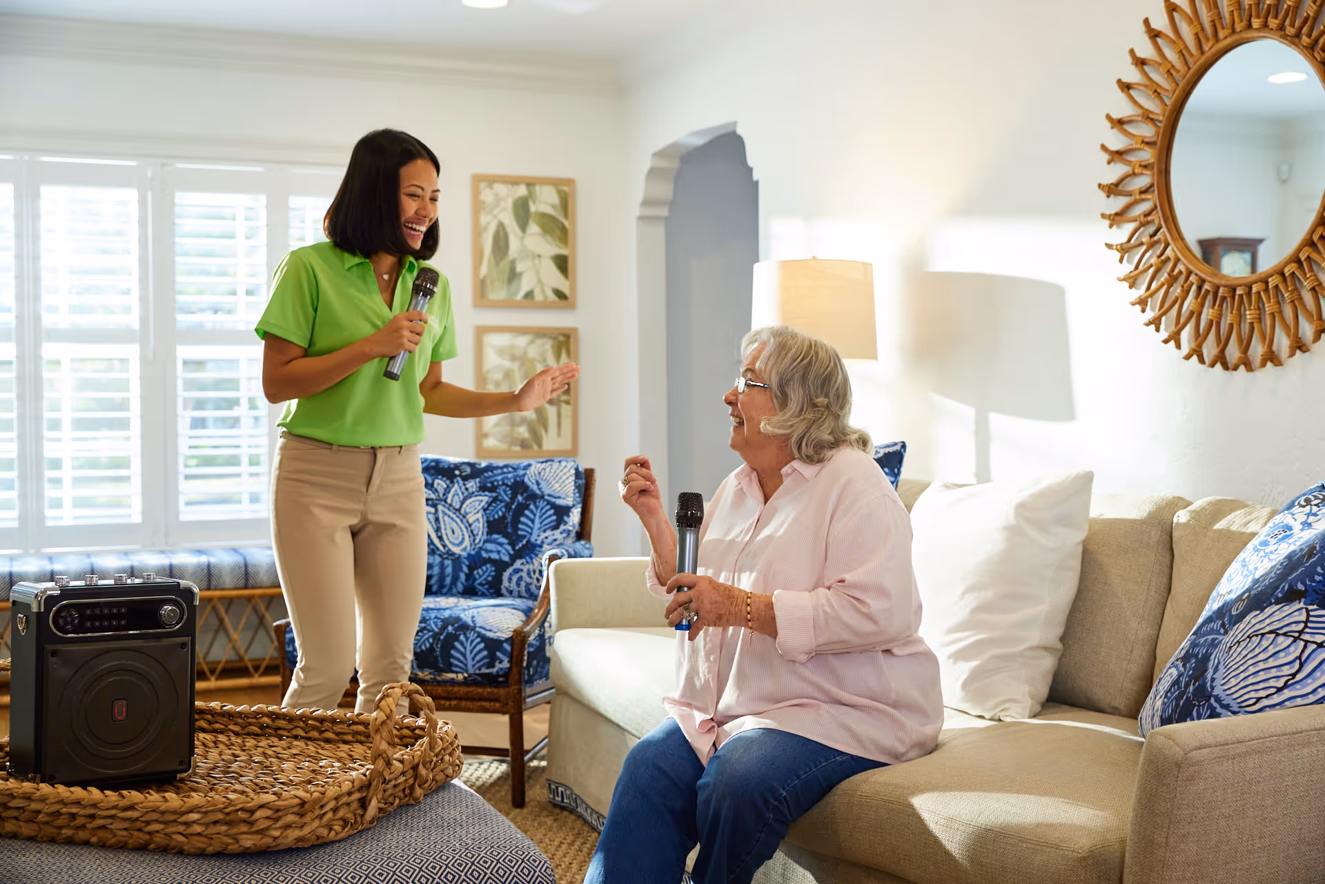 Caregiver and resident sing with microphones in a bright, cozy living room.
