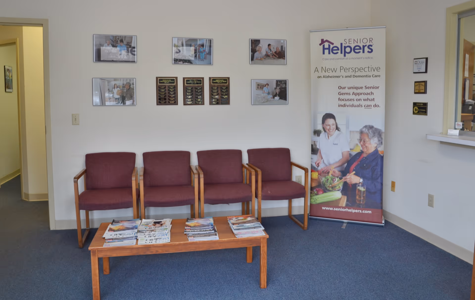 Waiting area with four purple chairs, a coffee table of magazines, and a Senior Helpers banner.