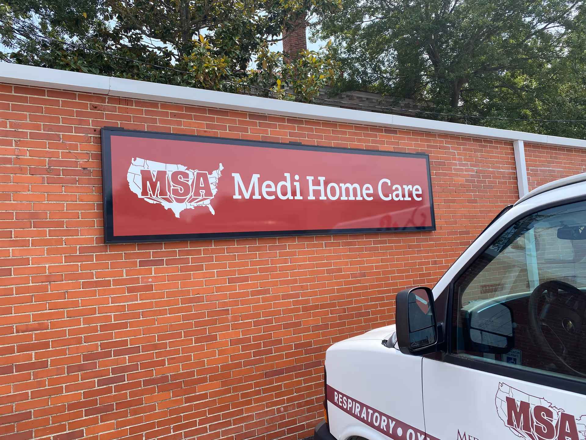 Red brick wall with a large Medi Home Care sign and a white van in front.