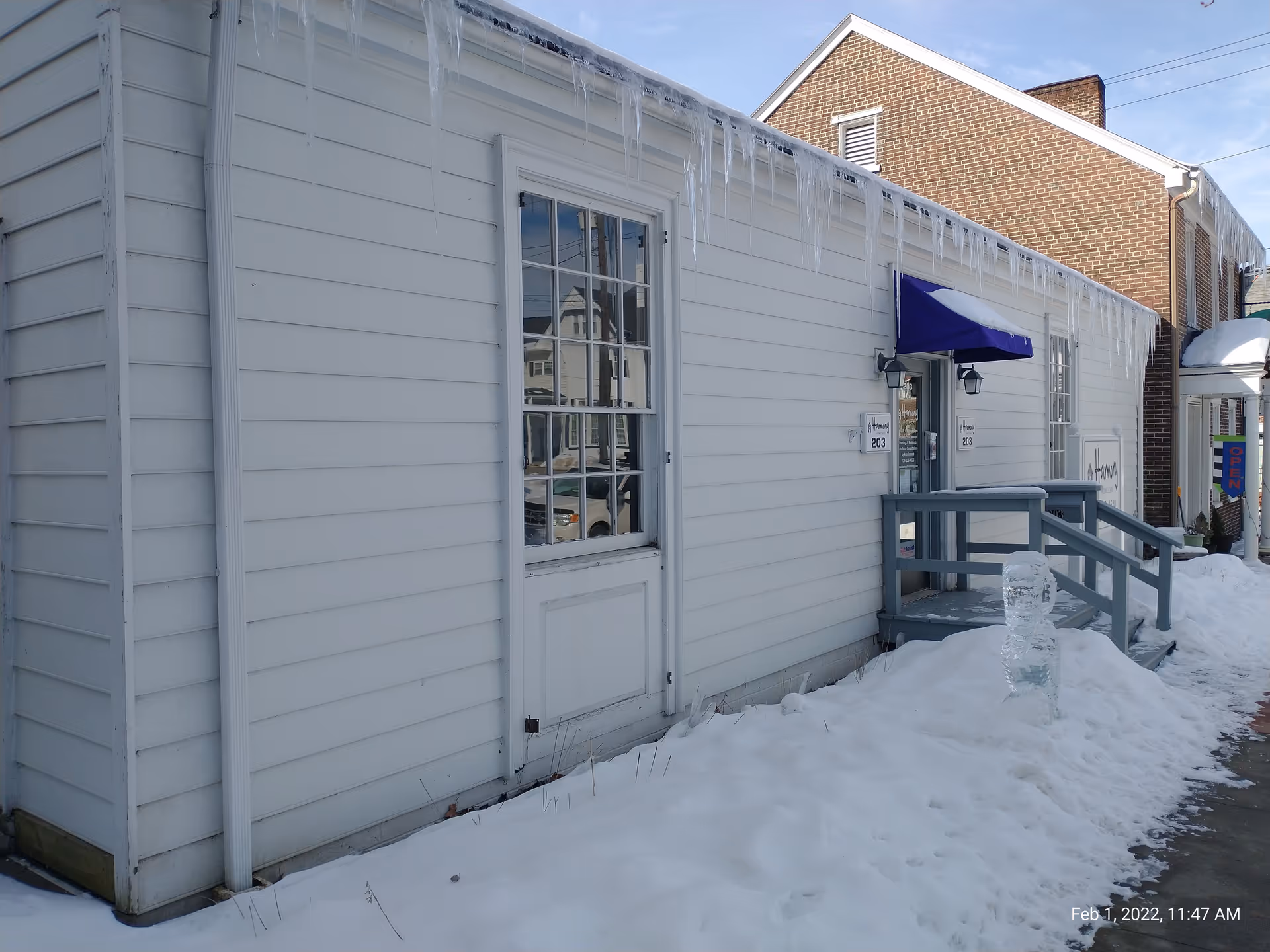 White exterior of a small building with stairs, icicles, and snow outside.