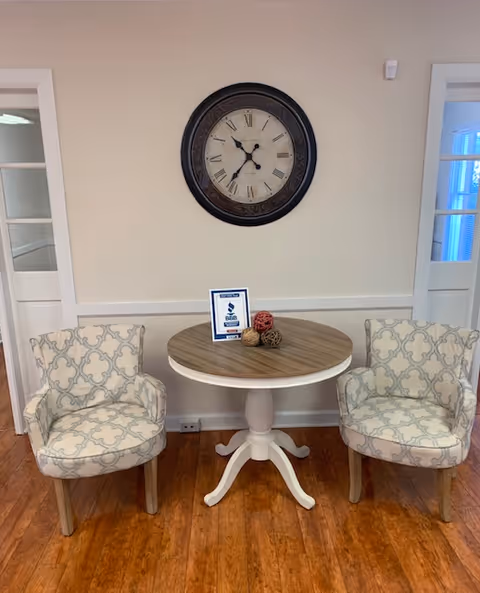 Two patterned chairs flank a round table beneath a wall clock in a cozy hallway.