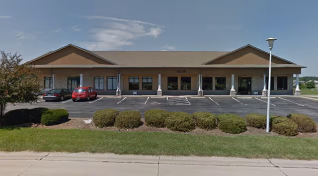 A single-story brick facility with a parking lot and landscaped shrubs in front.