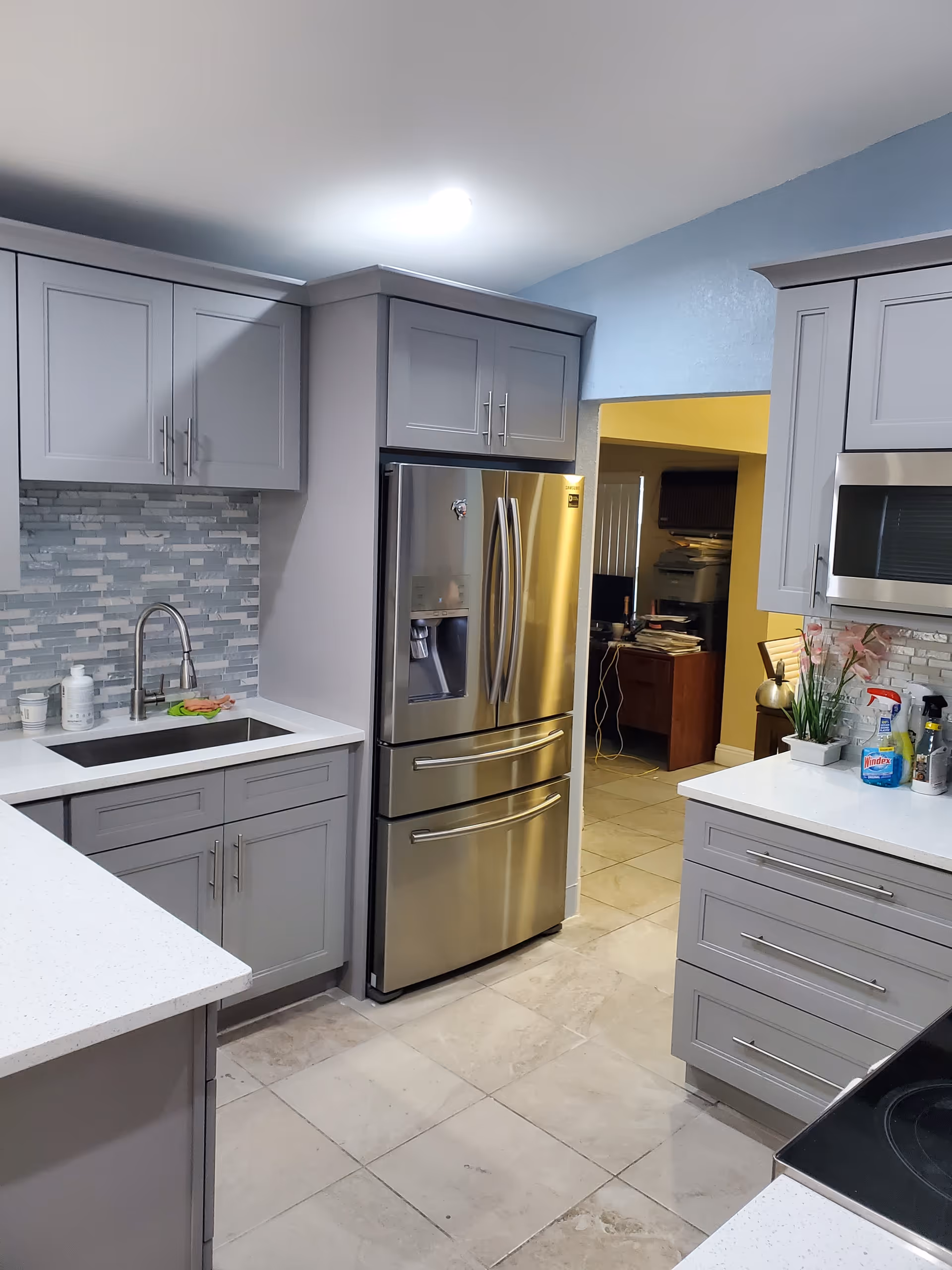 Modern gray kitchen with stainless steel fridge, sink, and white quartz countertops.