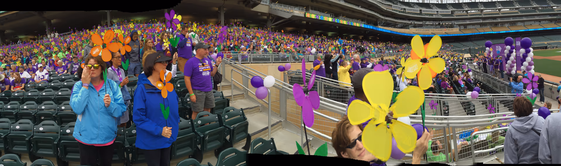 Crowd in a stadium holds colorful flower props at an outdoor event