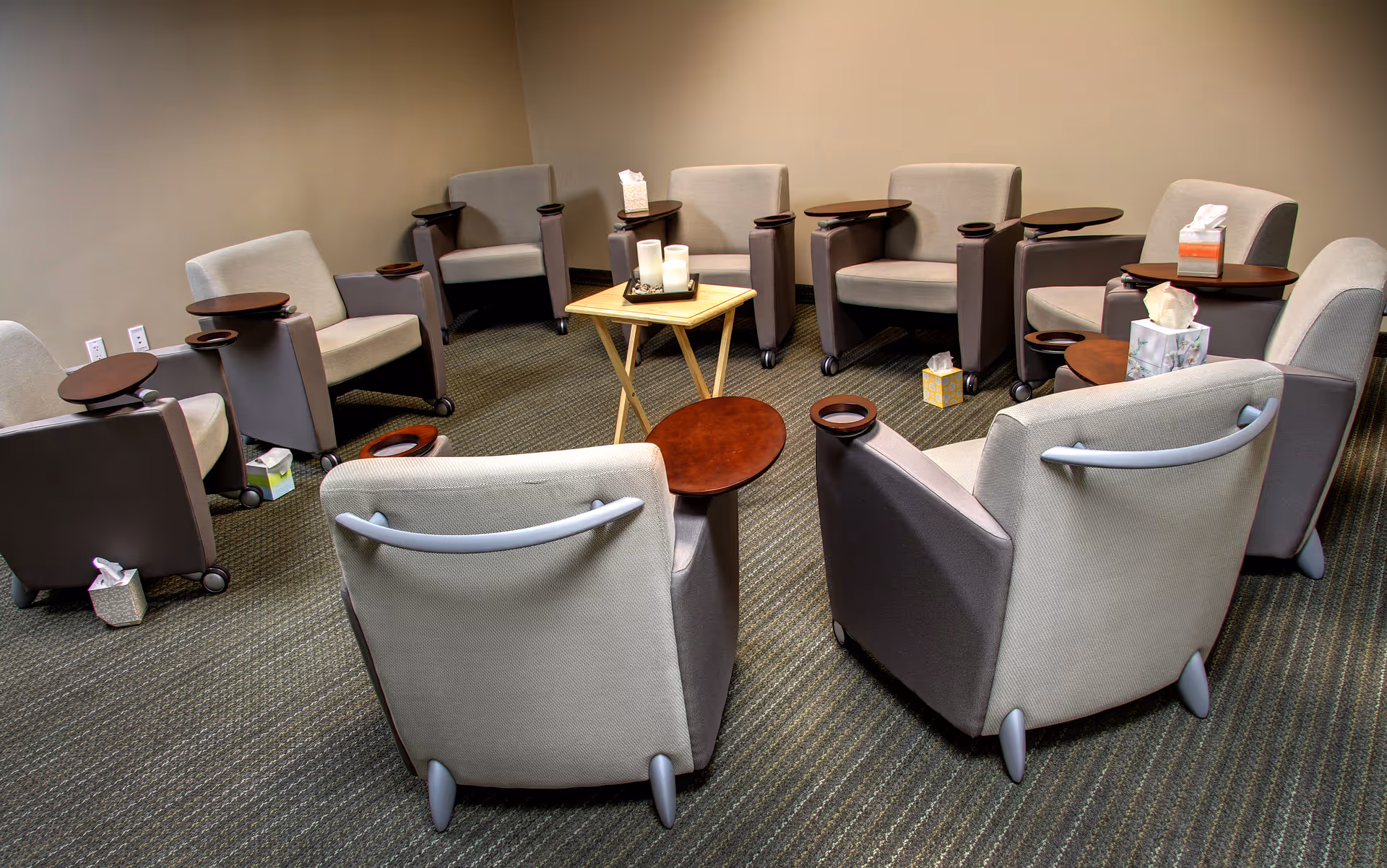 Circular seating lounge with grey chairs around small tables in a quiet waiting area
