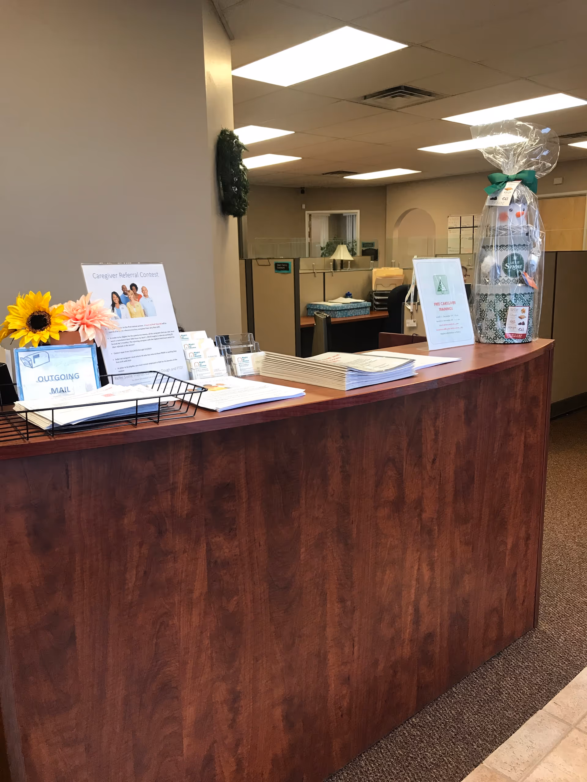 Wooden reception desk in a lobby with papers, signs, and a gift basket.