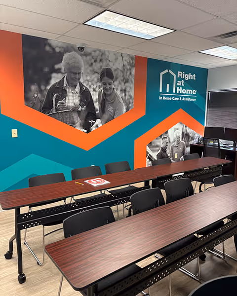 A training room with long desks, black chairs, and a colorful Right at Home mural.