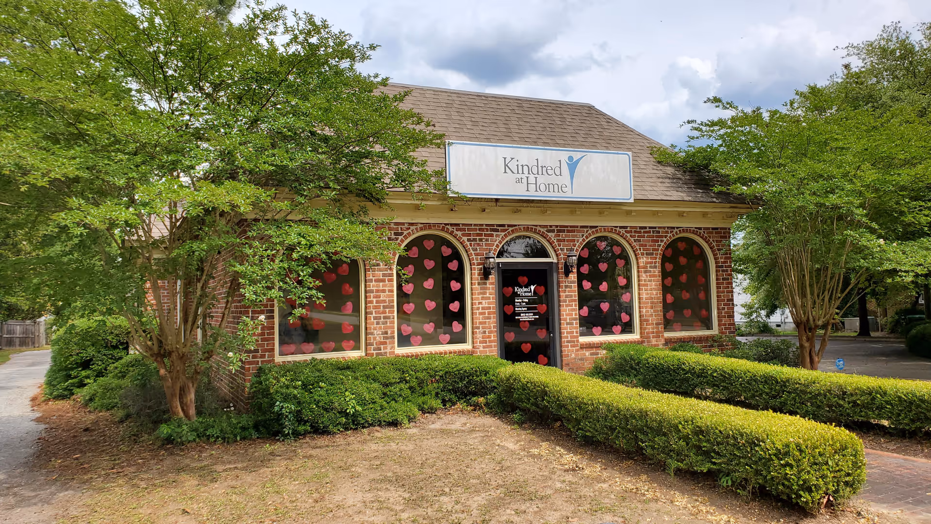 Brick building with arched windows, heart decorations on glass, and a Kindred at Home sign.