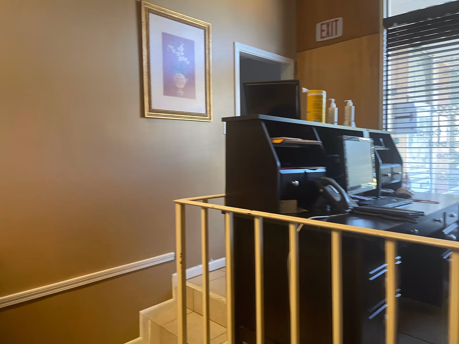 Interior reception desk with computer, sanitizer, and exit sign in a warm lobby.