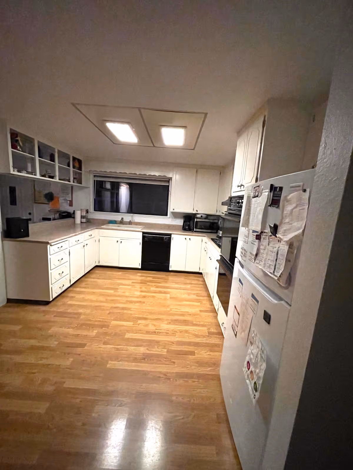 Bright white U-shaped kitchen with cabinets, appliances, and a wooden floor.