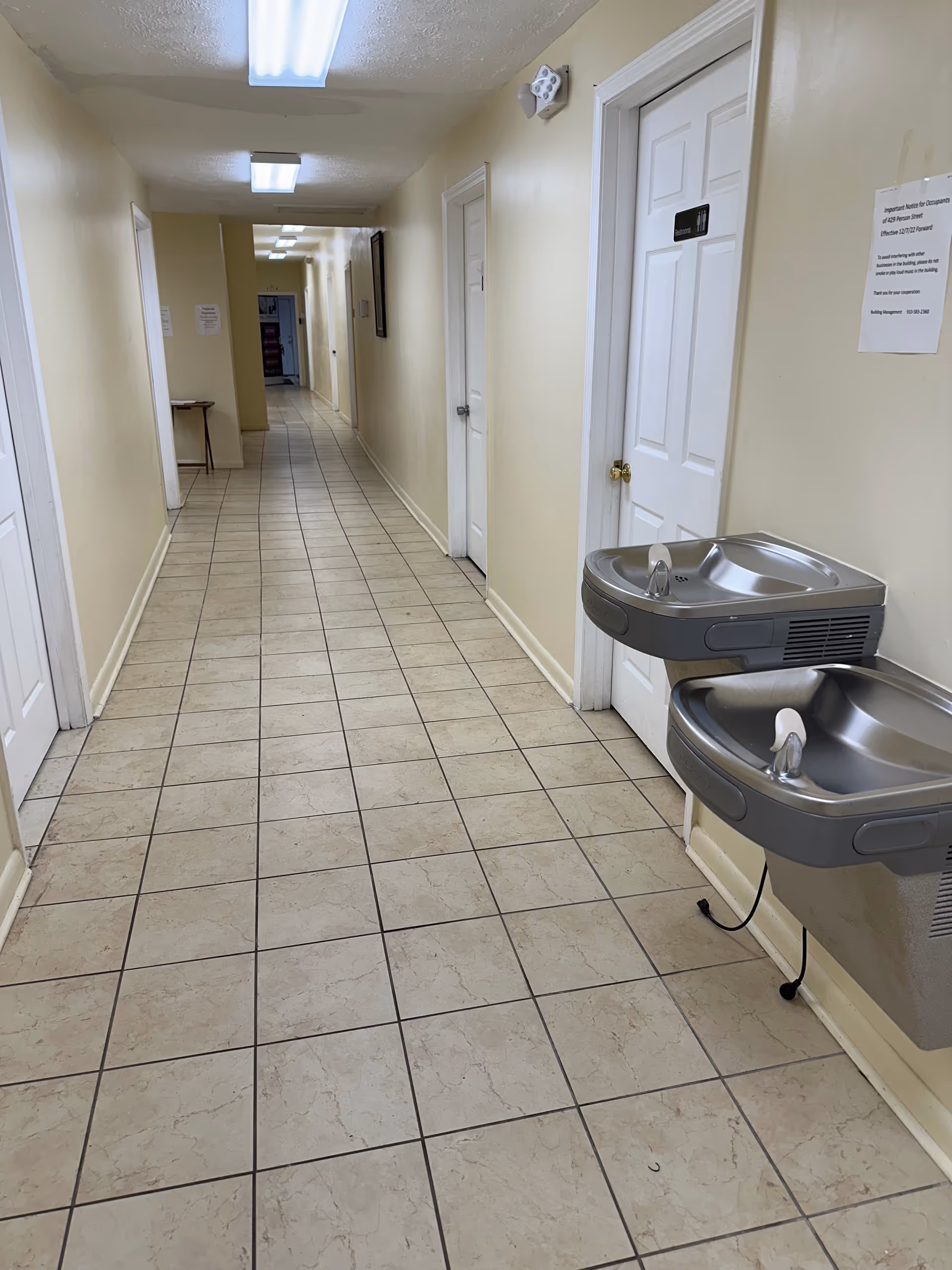 Empty hallway in a senior living facility with tiled floor and a fountain.