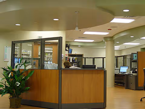 Interior reception area with a wooden curved desk, glass partitions, and a staff member.