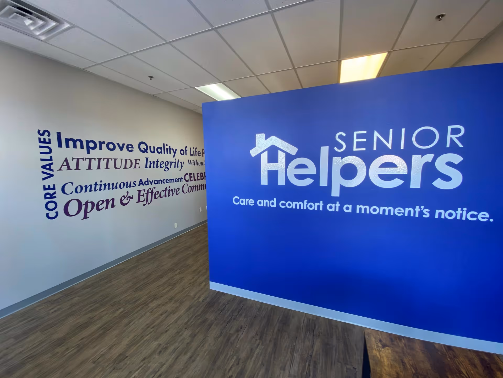 Bright interior hallway with blue Senior Helpers sign and motivational wall graphics.