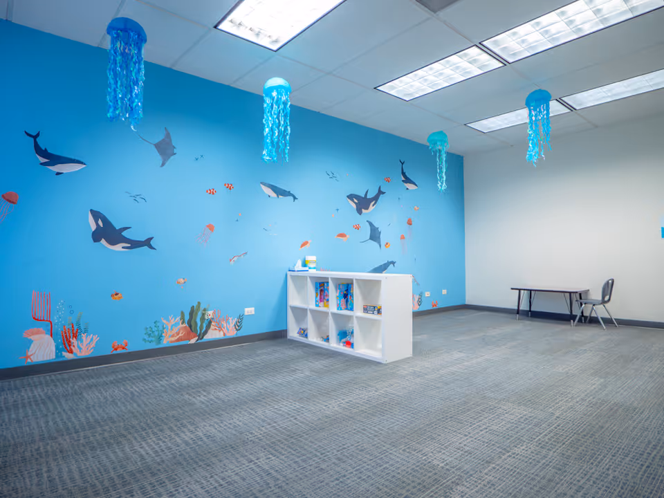 Interior activity room with blue ocean mural, ceiling lights, and white cubby shelf.