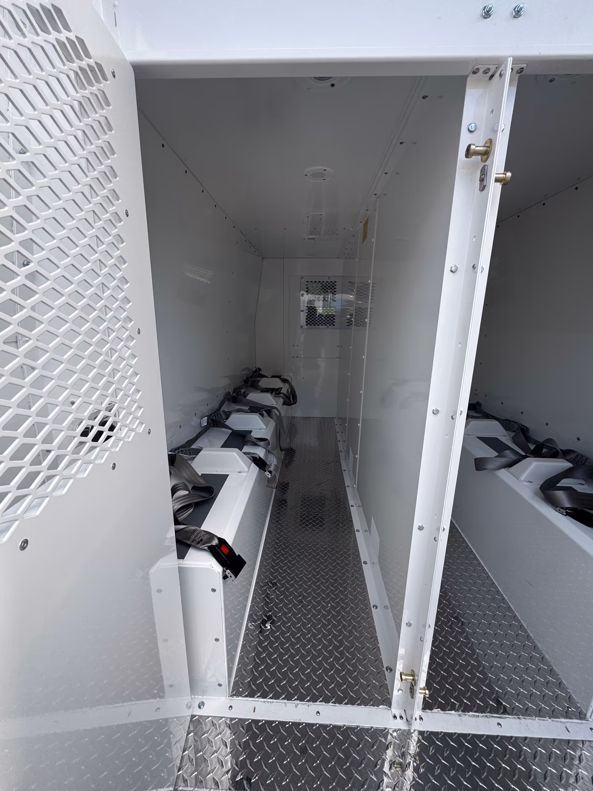 Interior of a white transport vehicle with diamond-plate floor and belt-secured seats.